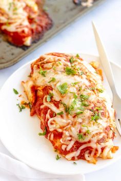 a white plate topped with lasagna covered in sauce and parmesan cheese