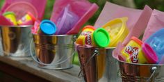 three buckets filled with play doh on top of a wooden table next to trees