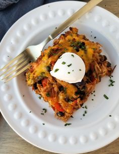 a white plate topped with an enchilada covered in cheese and sour cream