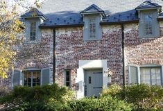 an old brick house with shutters on the front and side windows, surrounded by shrubbery