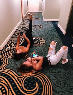 two young women laying on the floor with their cell phones in front of them,