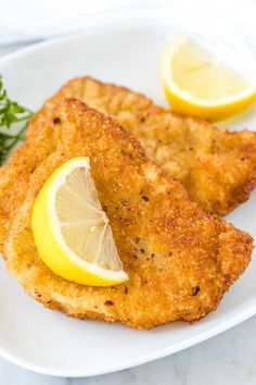 two fried fish fillets on a white plate with lemon wedges and parsley