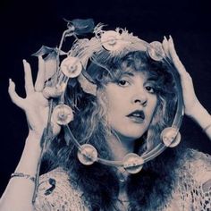 black and white photograph of a woman with flowers in her hair holding a flower crown over her head