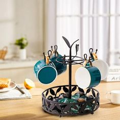 a cup holder with cups and spoons hanging from it's sides on a table