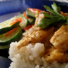 a blue plate topped with rice covered in sauce and veggies next to cucumbers