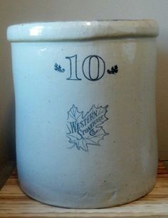 a large white pot sitting on top of a wooden table next to a wall and a clock