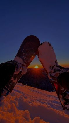 two snowboarders are standing in the snow at sunset with their feet propped up