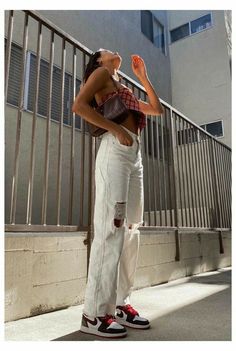 a woman standing on the sidewalk with her hands in her pockets and wearing ripped jeans