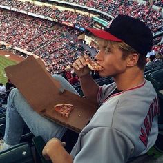 a young man eating pizza at a baseball game