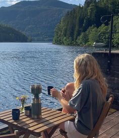 a woman sitting at a wooden table next to a lake