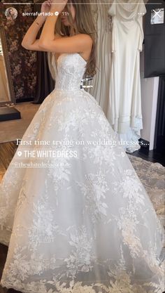 a woman in a white wedding dress looking at her cell phone while standing in front of a mirror