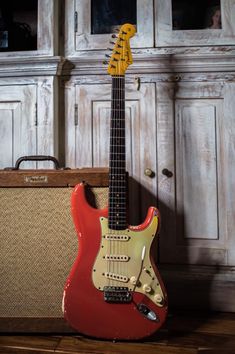 a red electric guitar sitting on top of a wooden table next to an old amp