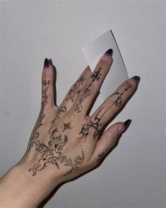 a person's hand with tattoos on it holding up a piece of white paper