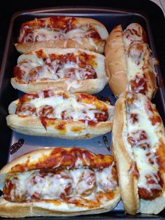 several hot dogs in buns covered with cheese and sauce on a baking sheet, ready to be eaten