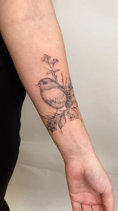 a person with a bird tattoo on their arm holding onto a flower and leaves bracelet