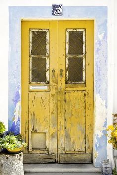 an old yellow door in front of a blue and white building with potted plants