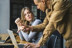 a man and woman sitting at a table with their hands clasped over the keyboard of a laptop