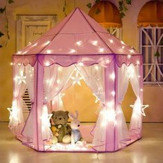 a teddy bear sitting in a pink tent with fairy lights