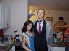 a man and woman standing next to each other in a kitchen with clutter on the counter