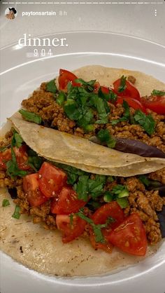 two tacos are sitting on a plate with tomatoes and cilantros in it