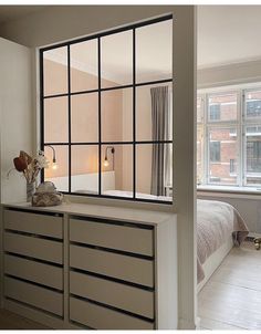 a bedroom with a bed, dresser and large window in the wall next to it