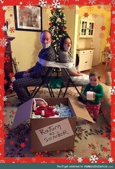 two adults and a child sitting in front of a christmas tree with a sign on it