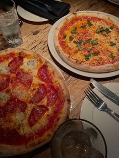 two pizzas sitting on top of white plates next to silverware and utensils