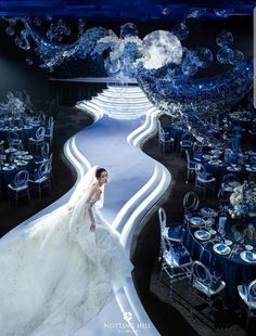 a woman in a wedding dress standing next to a table with blue chairs and tables