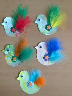 four little birds made out of paper with colorful feathers and flowers on their heads, sitting next to each other