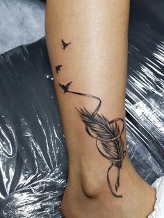 a woman's foot with a tattoo on it that has birds flying around the feather