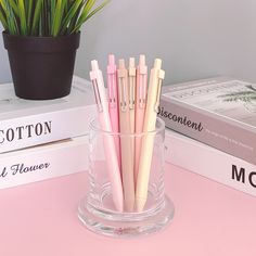 several pens are in a glass cup on a table next to books and a potted plant