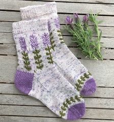 two socks with purple flowers on them sitting next to a sprig of rosemary