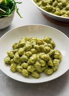 a white bowl filled with green food next to another bowl full of spinach leaves