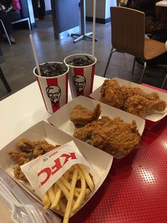 three trays of fried chicken and fries on a table with two cups of soda