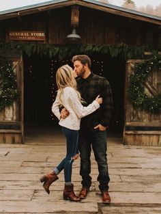 a man and woman standing in front of a building with christmas lights on the roof