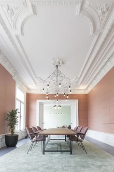 an empty conference room with pink walls and white trim on the ceiling, chandelier and chairs