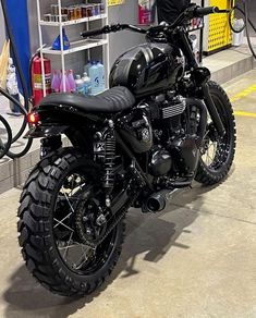 a black motorcycle parked in a garage next to a shelf filled with bottles and other items