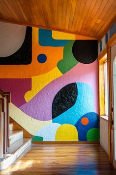 an empty room with colorful painted walls and wooden floors in front of a doorway that leads to the second floor