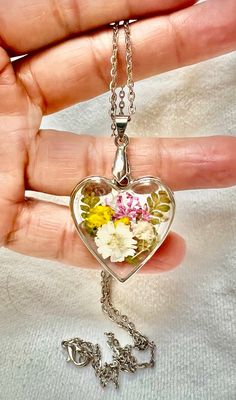 a person holding a heart shaped necklace with flowers in it and the word love written on it