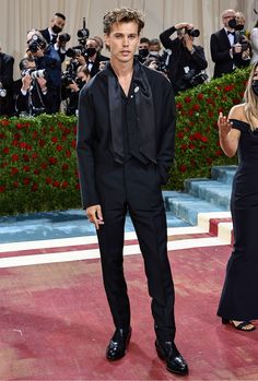 a man in a tuxedo standing on a red carpet with cameras around him