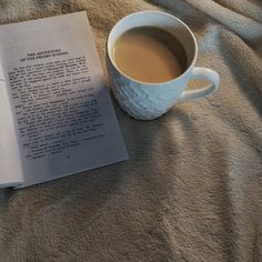 a cup of coffee and an open book on a bed with the pages spread out