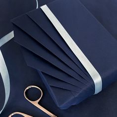 a pair of scissors and some blue paper with white ribbon on it next to a pair of gold scissors