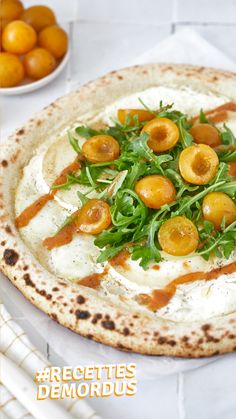 a pizza topped with cheese and veggies on top of a white plate next to oranges