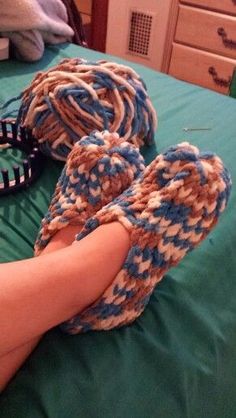 someone's feet with crocheted slippers on top of a green bed