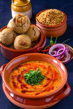 three bowls filled with food on top of a blue table next to onion and bread