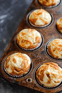 a muffin tin filled with orange and white cupcakes covered in icing