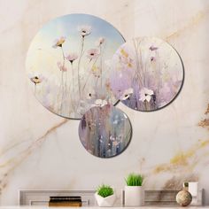 three circular paintings hanging on the wall above a table with vases and plants in front of it