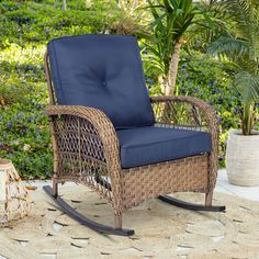 a wicker rocking chair with blue cushions on a rug in front of some plants