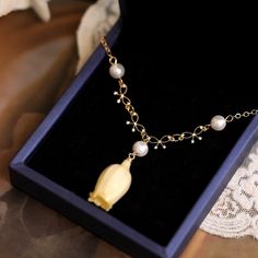 a necklace in a box with pearls on the chain and a flower charm hanging from it