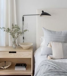 a bed with white sheets and pillows next to a wooden nightstand topped with a potted plant